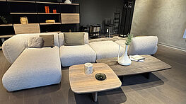 The Freifrau Mia sofa in beige fabric can be arranged in many different ways with a recamier and pouf, and is now available at a reduced price in the design sale at Grünbeck Einrichtungen.